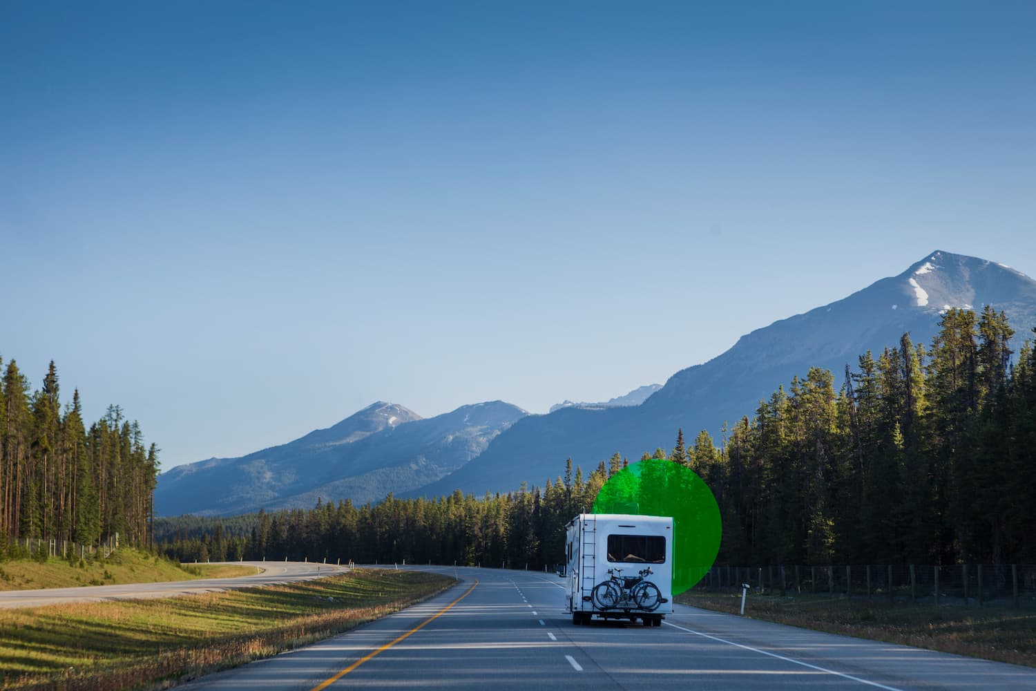 White and gray Class A motorhome driving on desert highway surrounded by scrub brush and arid terrain
