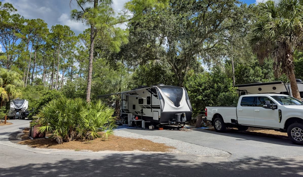 White and gray Class A motorhome driving on desert highway surrounded by scrub brush and arid terrain