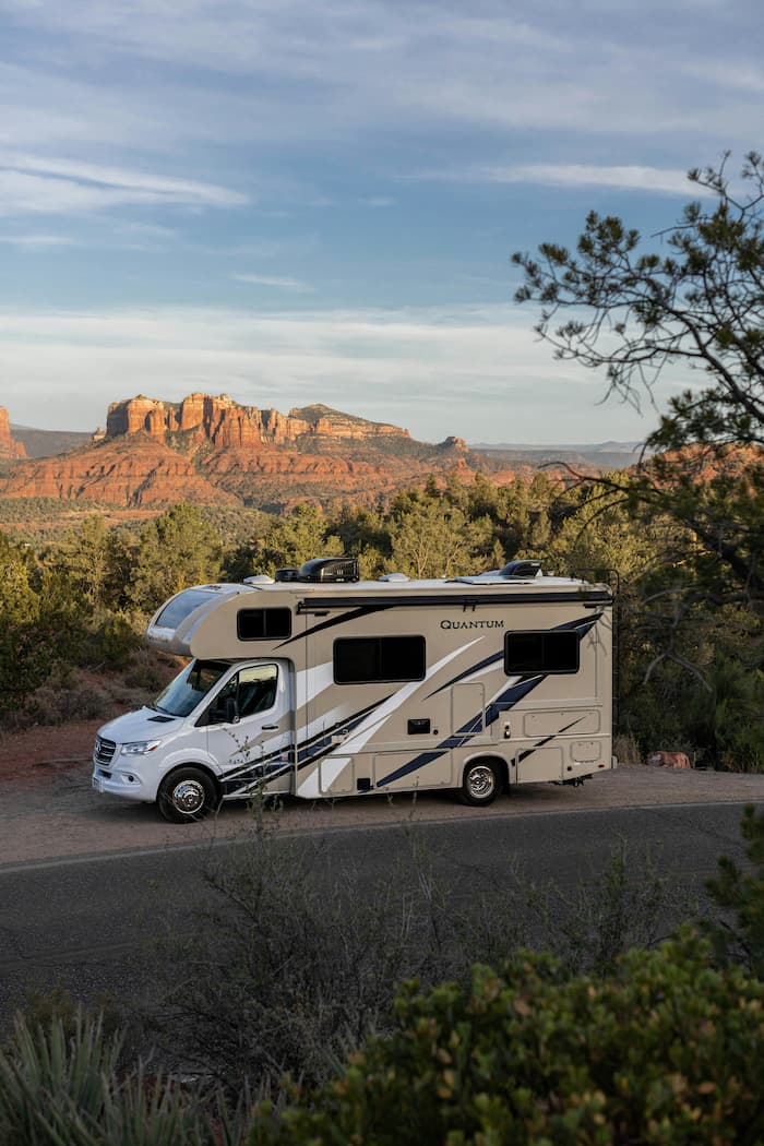 Large motorhome parked among tall evergreen trees in mountain forest