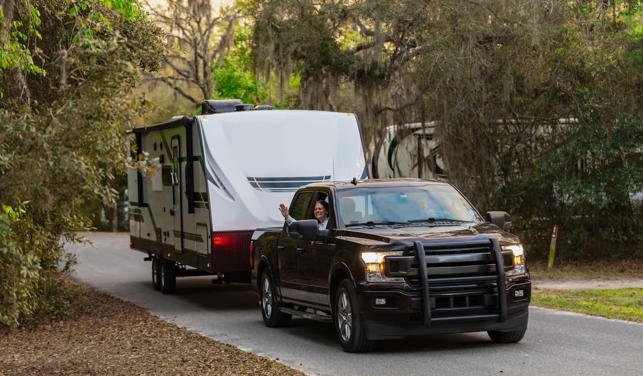 Black pickup truck with camper attachment positioned on sandy desert terrain with red rock formations in background