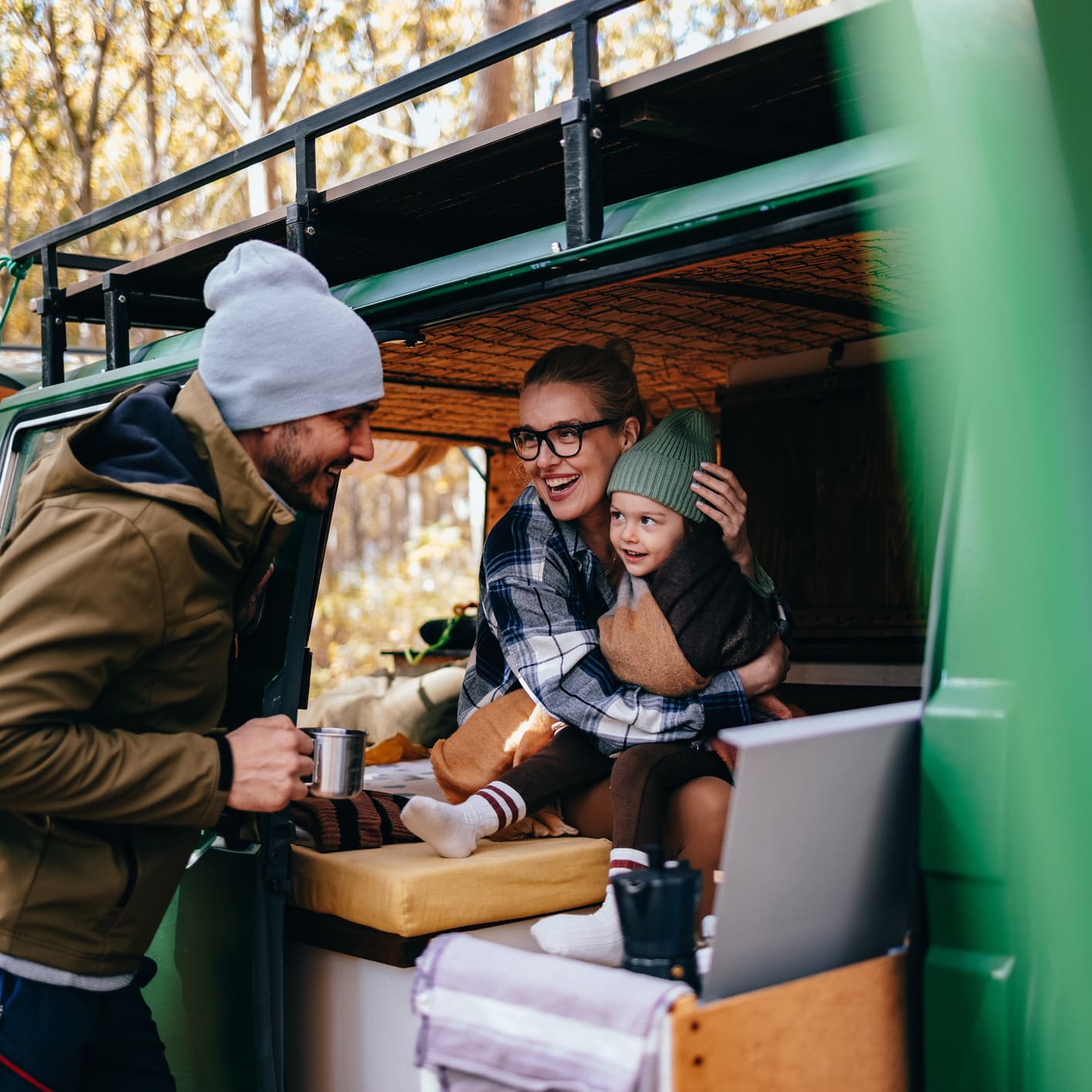 A woman sitting in a camper van holding a toddler while laughing with a man