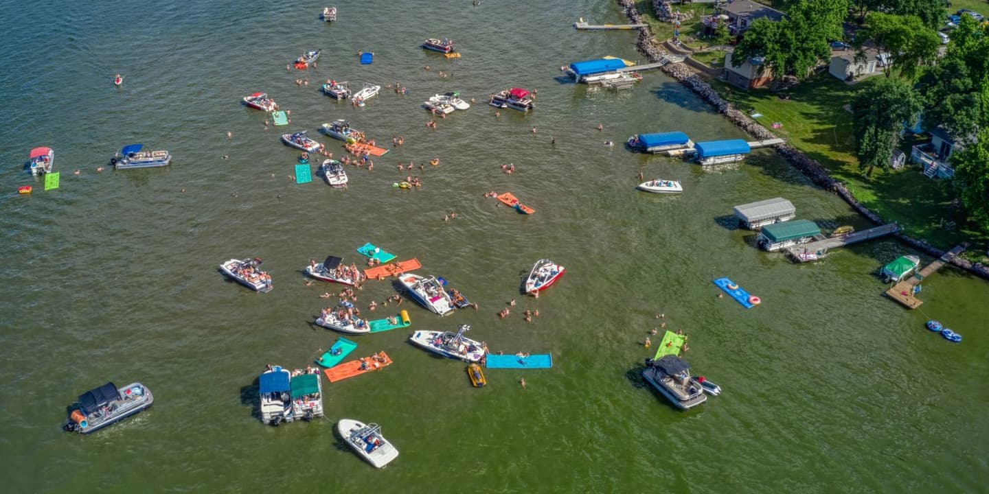 Aerial view of boats and people swimming on colorful floating mats in a lake, a popular setting for those with South Dakota boat insurance.