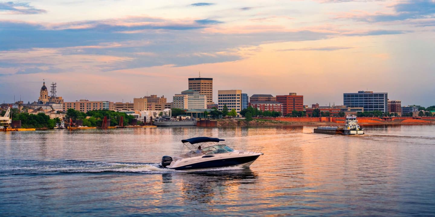 A motorboat cruises on an Indiana river against a city skyline at sunset.