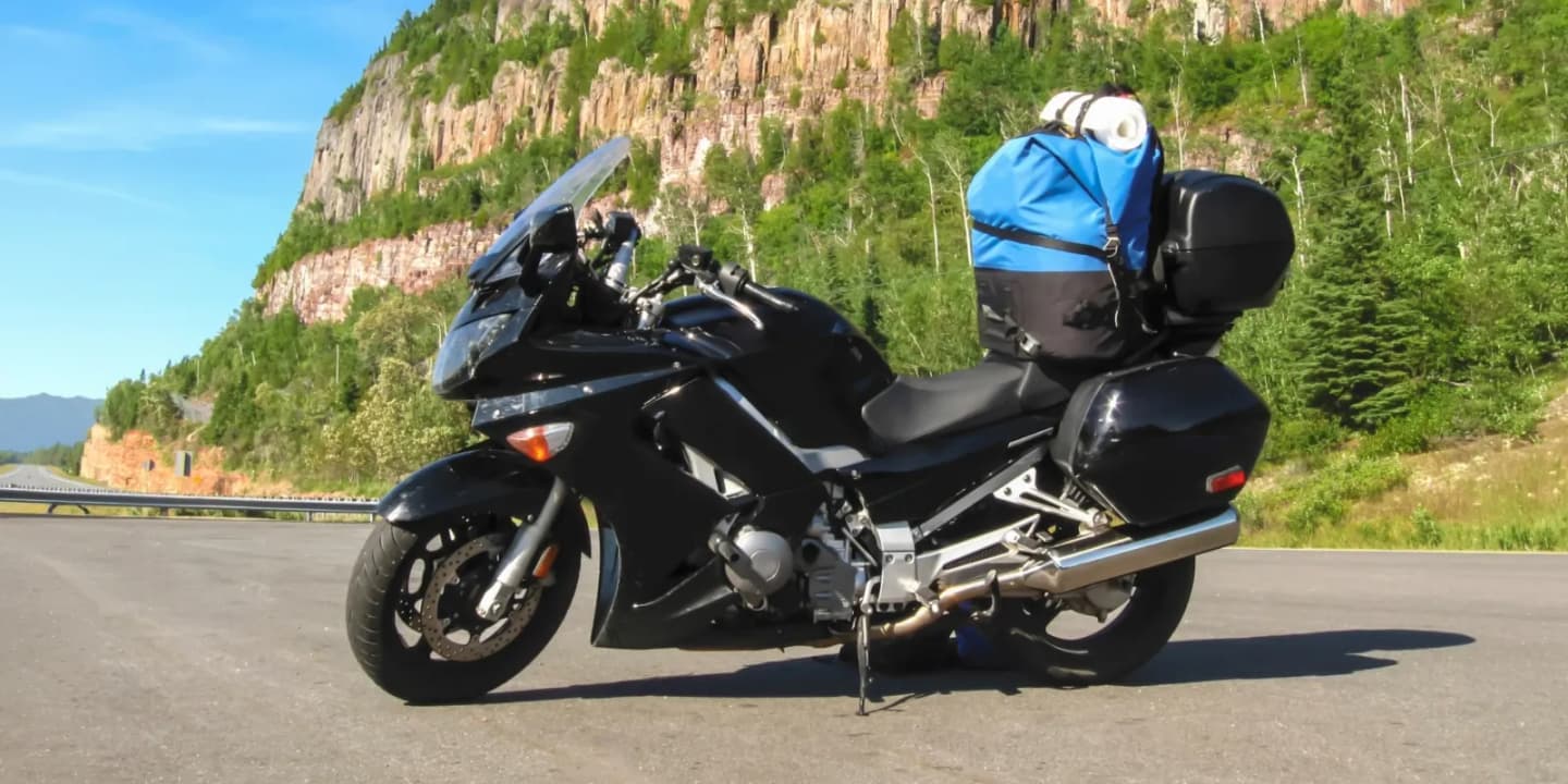 Black touring motorcycle with luggage and storage cases parked along a scenic mountain road