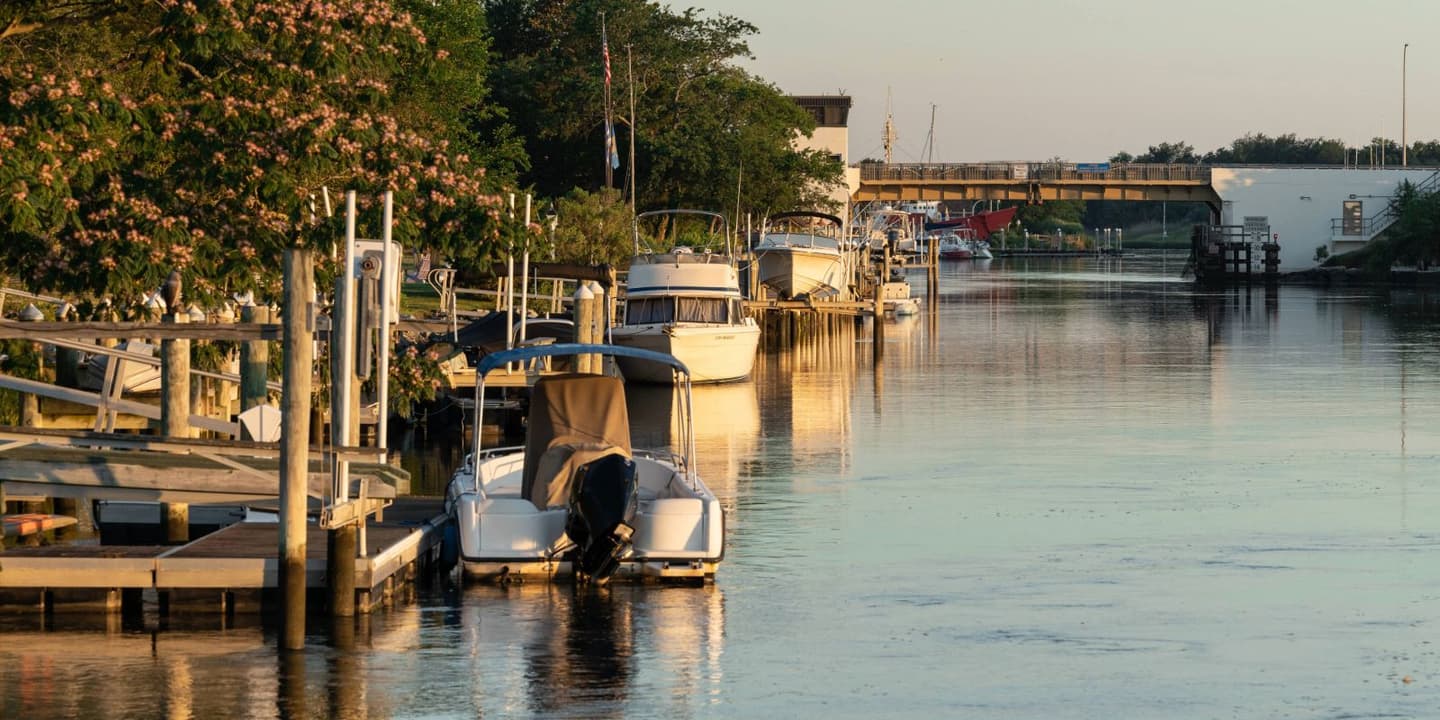 Small boats requiring Delaware boat insurance are moored along docks in a canal leading toward a drawbridge.