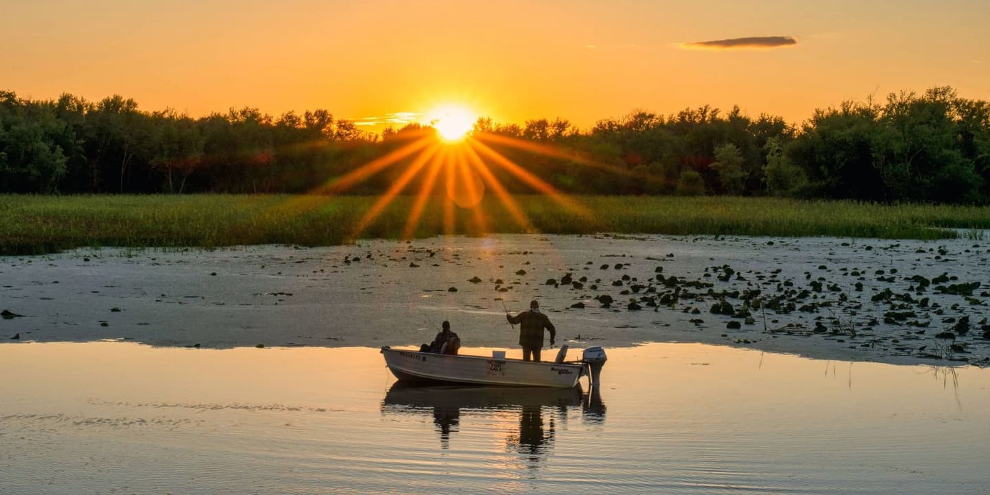 Two people in a small motorboat fishing on a lake at sunset, protected by Wisconsin boat insurance.