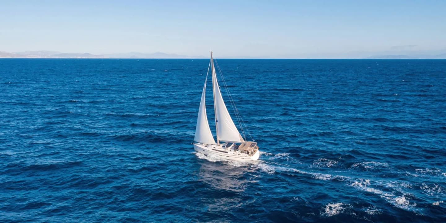 White sailboat cruising across deep blue ocean waters with sails raised