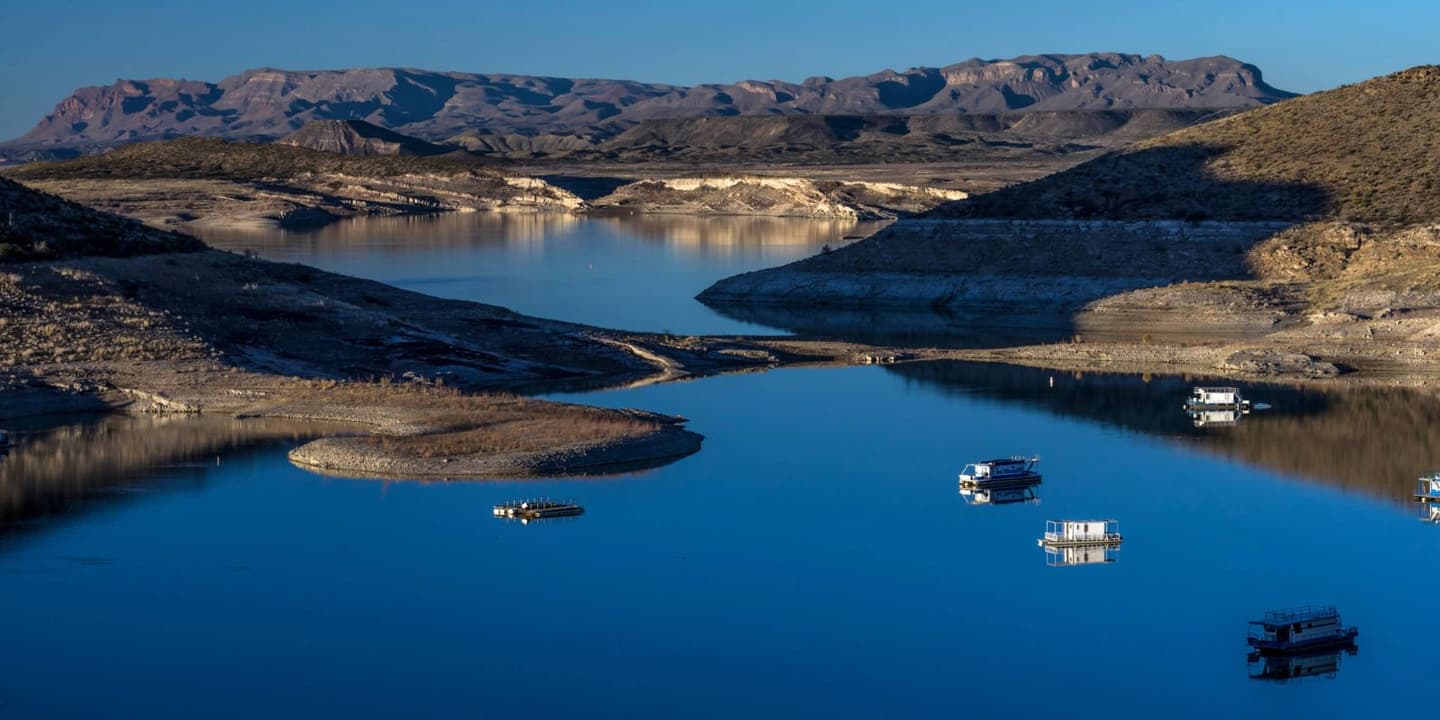 Several boats, protected by reliable New Mexico boat insurance, float on the calm blue water of a reservoir surrounded by arid hills and distant mountains.