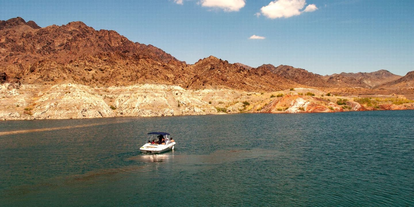 A white motorboat with a blue canopy floats on a large lake in Nevada, set against a backdrop of arid, rocky mountains.