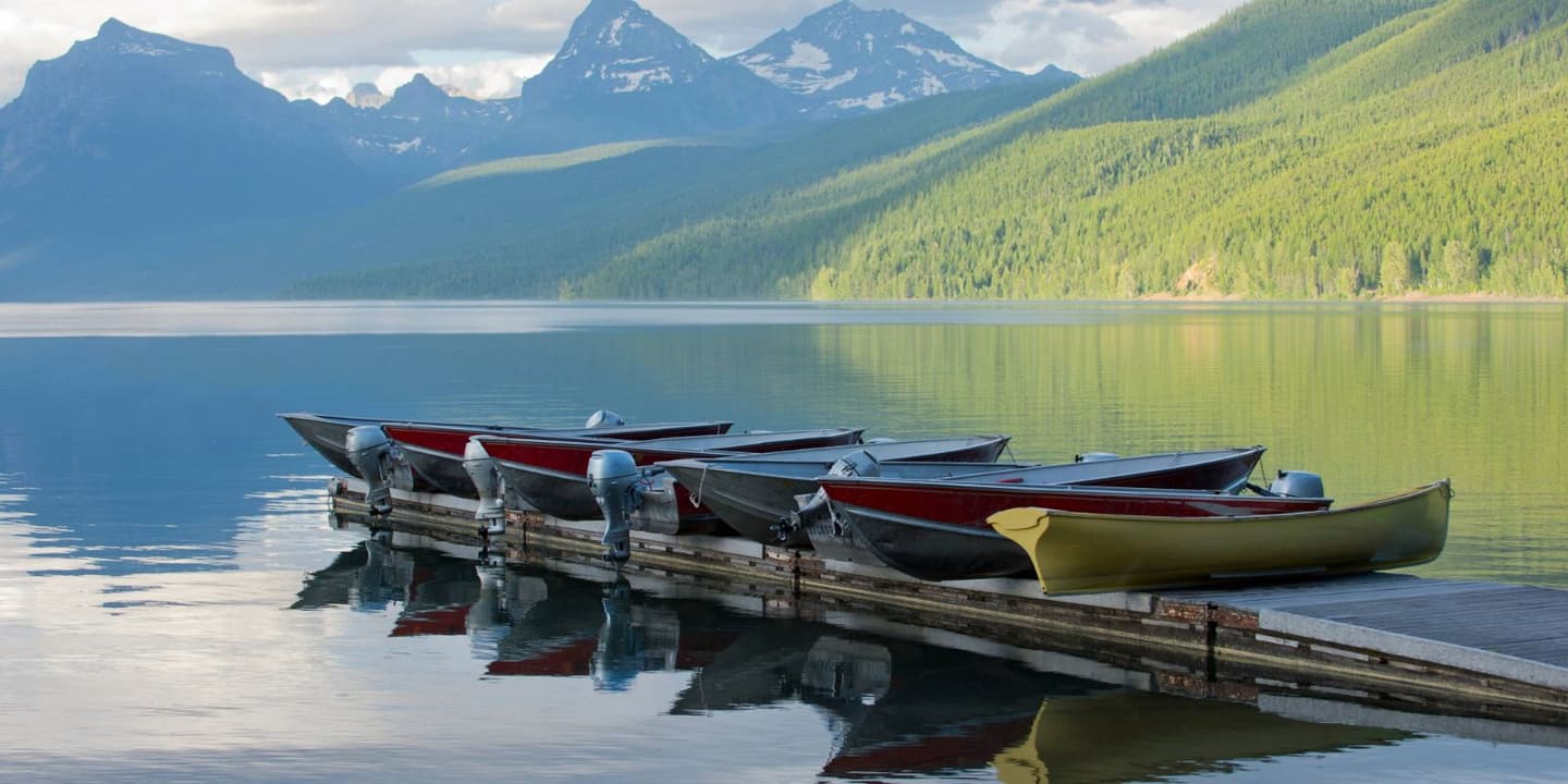 A row of small motorboats docked at a wooden pier on a calm lake with mountains in the background