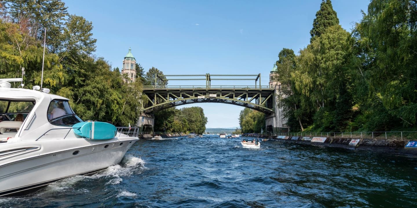 A white motorboat, the type often covered by Washington boat insurance, travels through a canal toward the George Washington Memorial Bridge, with smaller boats in the distance.