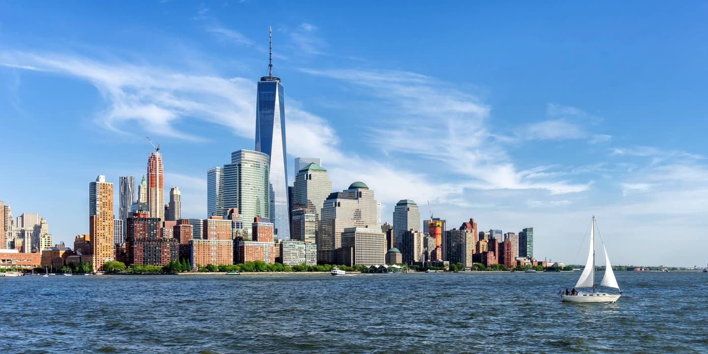 The Manhattan skyline featuring One World Trade Center viewed across the Hudson River with a sailboat in the foreground, reminiscent of scenes protected by New York boat insurance.