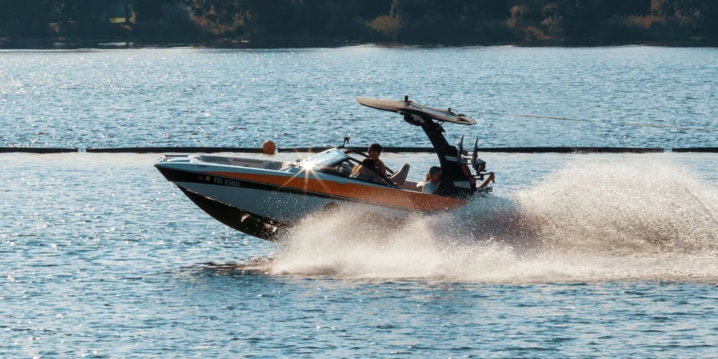 Ski and wake boat speeding across a lake with passengers and a raised wakeboard tower