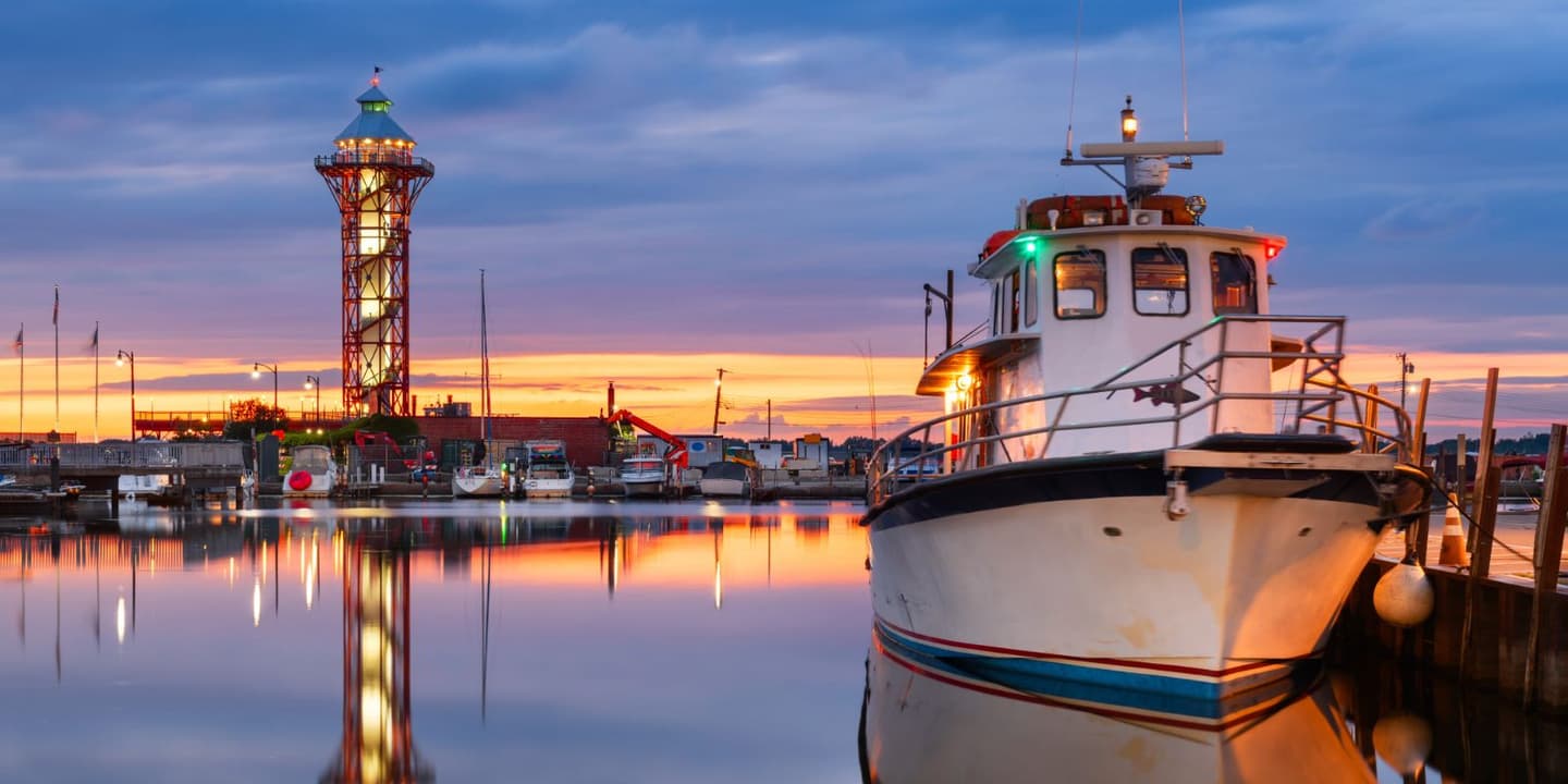 A motorboat docked at a harbor during sunset, near a setting where Pennsylvania Boat Insurance is essential, with a tall, illuminated observation tower reflecting in the calm water.