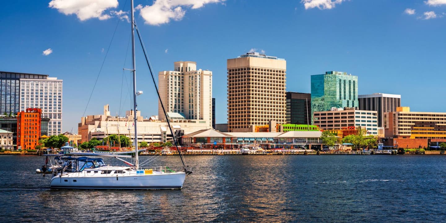 A sailboat on the water in front of a city skyline, representing the scenic coastal beauty often protected by Virginia Boat Insurance.