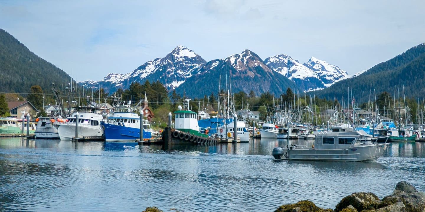 Fishing boats with Alaska boat insurance moored in a harbor with snow-capped mountains in the background.