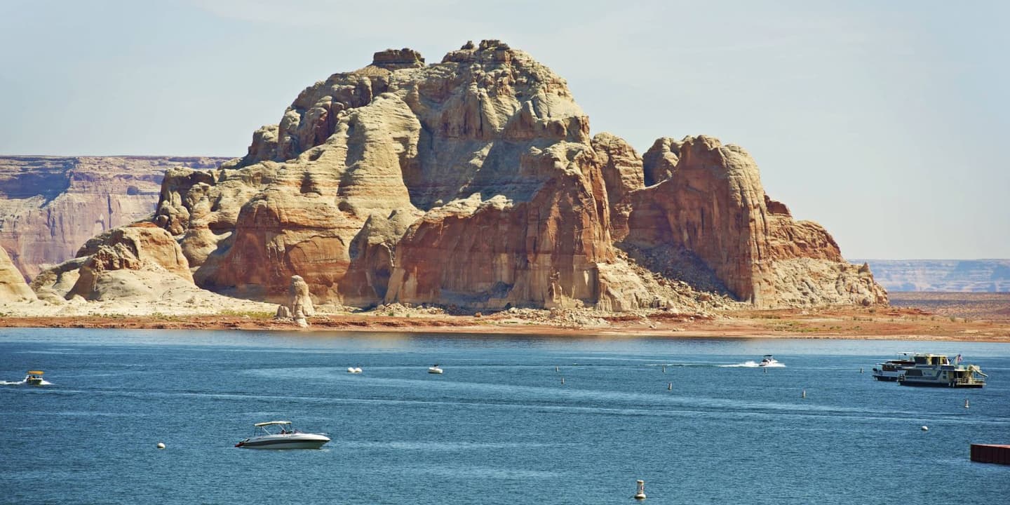 A large rock formation rising above Lake Powell near boats that might require Utah boat insurance.