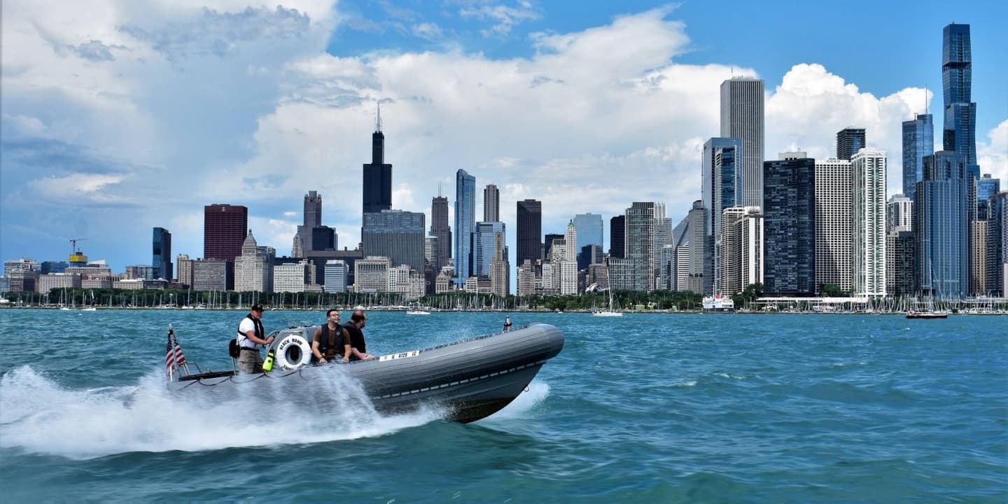 A rigid-hulled inflatable boat with three people on board speeds across the water toward the Chicago skyline, a common sight for Illinois boat insurance policyholders.