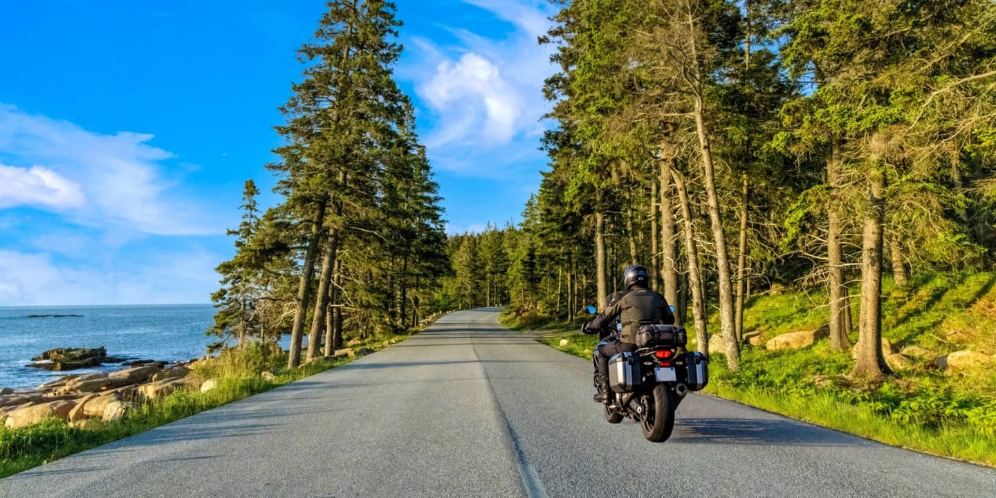 Motorcycle rider traveling along a scenic road in Maine